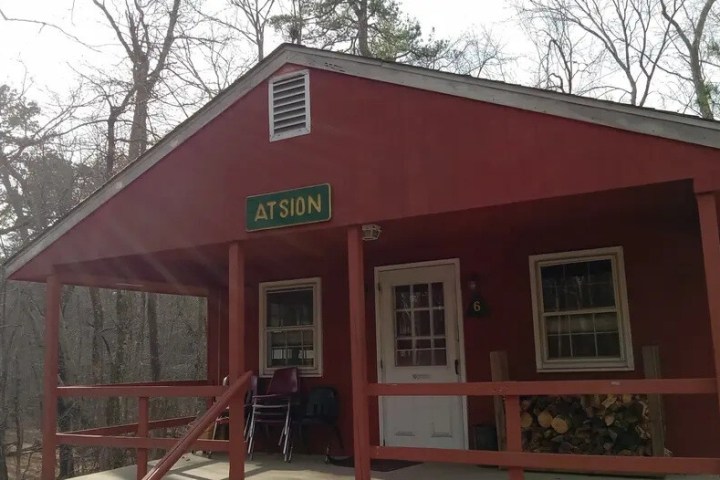 Red cabin with porch, white door, and sign reading 'ATSION' set in a wooded area.