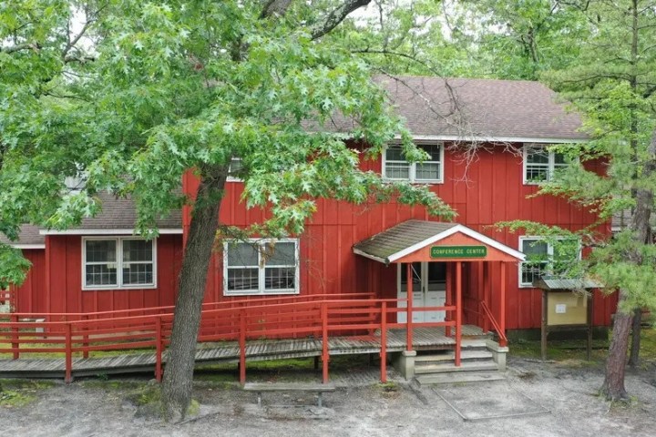 Red conference center building surrounded by trees with a ramp and steps leading to entrance.