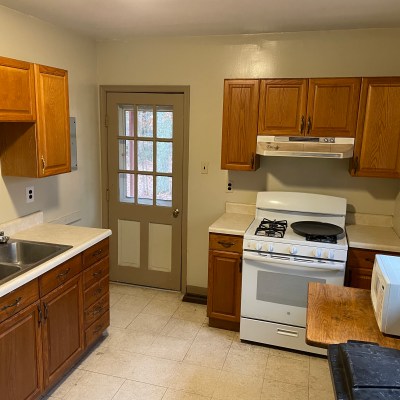 Small kitchen with wooden cabinets, stove, double sink, microwave, and door with window panels.