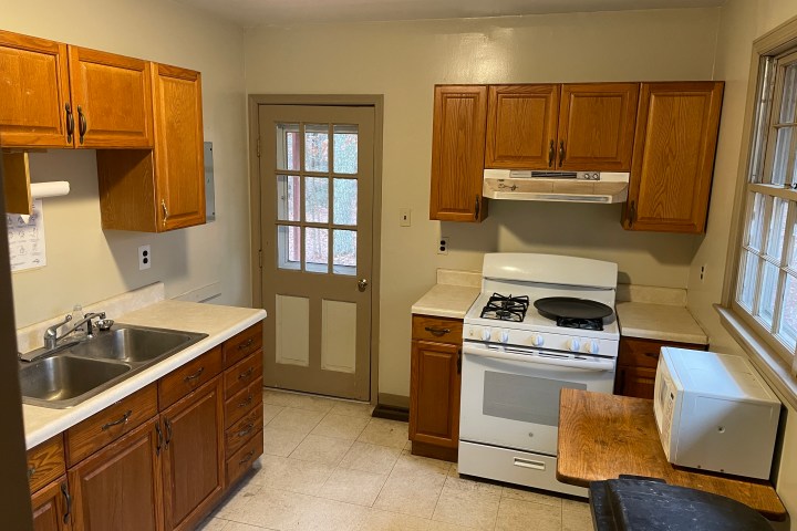 Small kitchen with wooden cabinets, stove, double sink, microwave, and door with window panels.