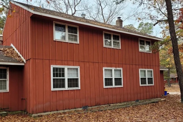 Two-story red house with multiple windows, surrounded by autumn trees and fallen leaves.