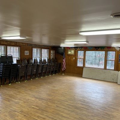 Empty room with stacked chairs, wooden floors, and American flag by the window.