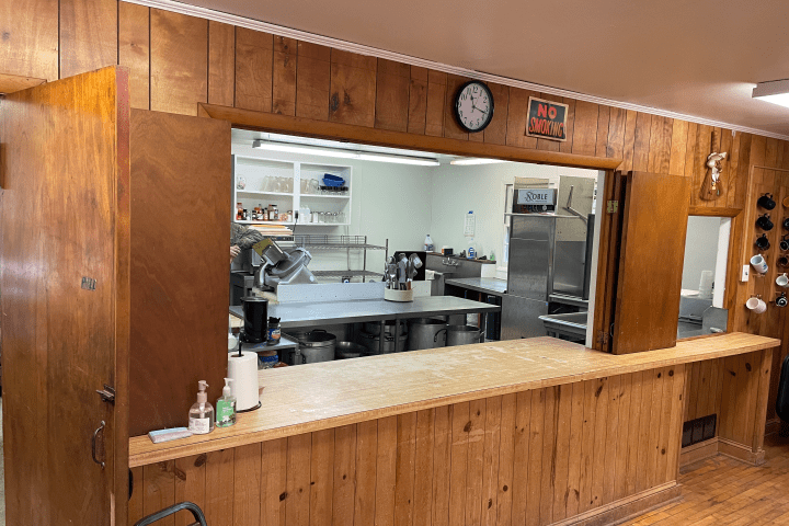 Wood-paneled interior with a serving counter and view into a commercial kitchen.