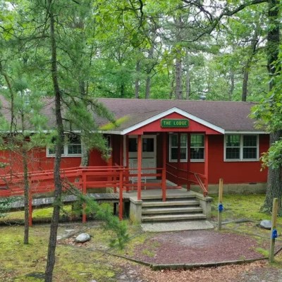 A red wooden lodge surrounded by trees with a sign reading 'The Lodge' above the entrance.
