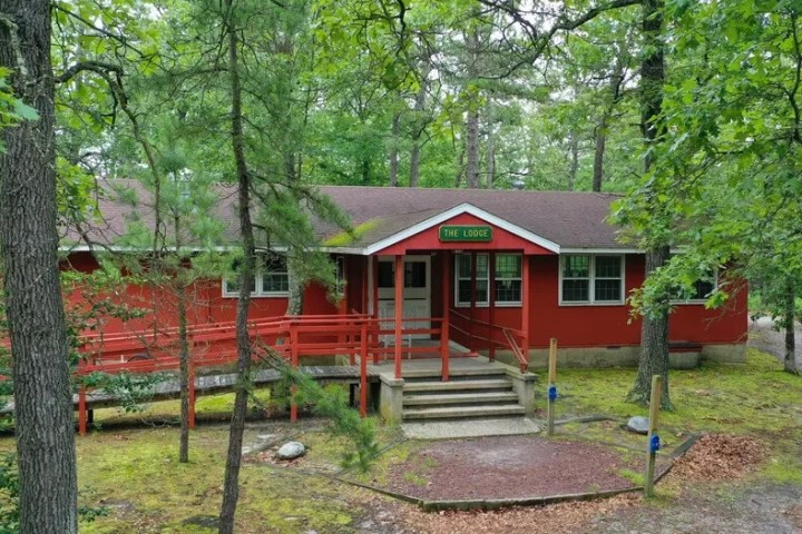 A red wooden lodge surrounded by trees with a sign reading 'The Lodge' above the entrance.