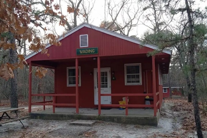 Red cabin labeled 'Wading' surrounded by leafless trees, with a picnic table in front.