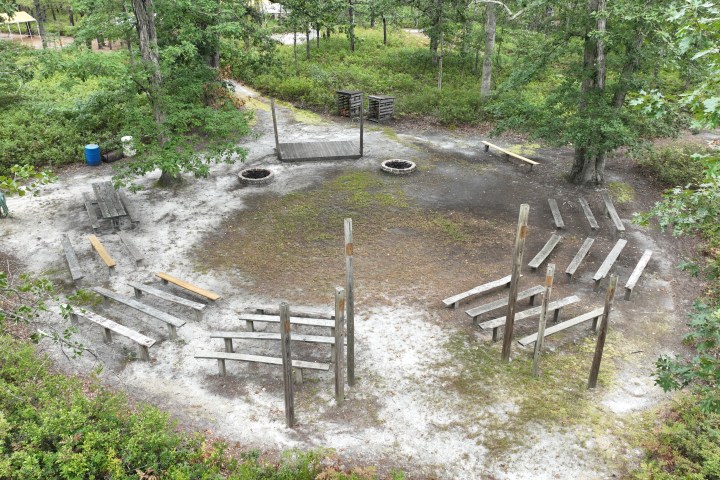 Outdoor amphitheater with wooden benches and a central fire pit in a forested area.