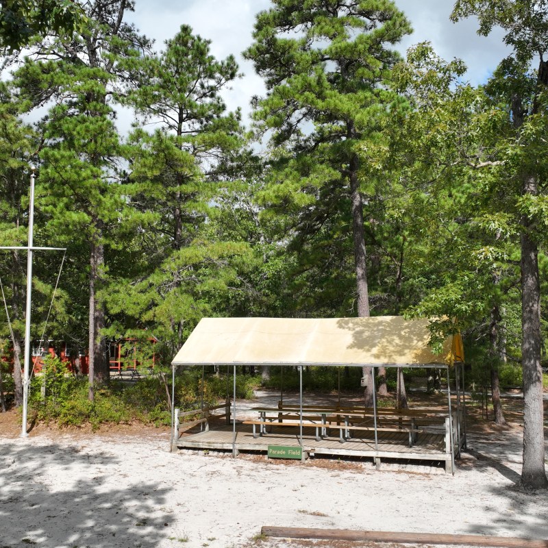 Wooden shelter with a beige canopy in a forested area on a sunny day.