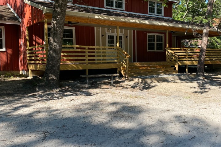 Red two-story house with a wooden porch and trees around.
