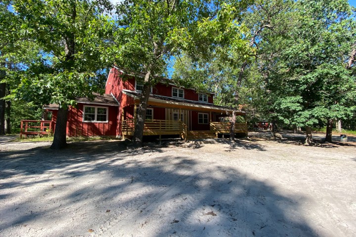 Rustic red cabin surrounded by trees under a clear blue sky.