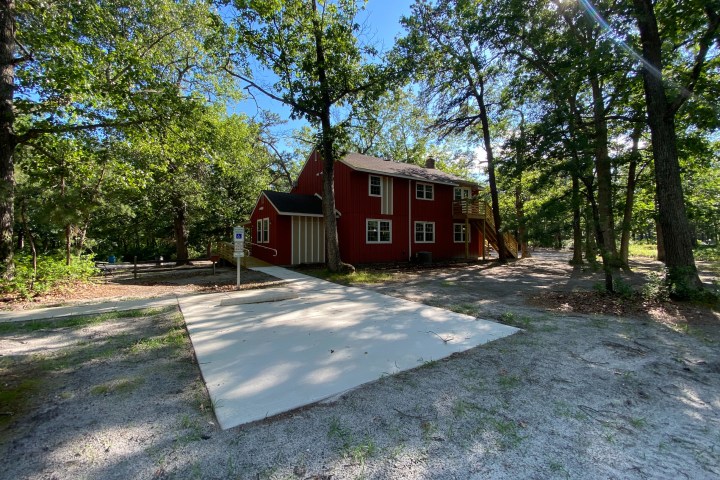 Red house surrounded by trees with a gravel and concrete driveway.