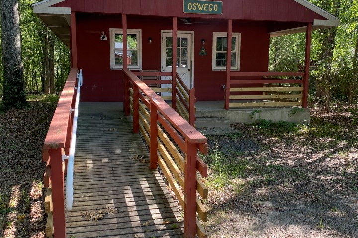 Red cabin with a wooden ramp in a forest setting.