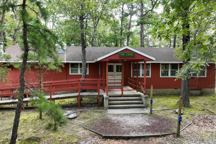 A red lodge in a forest setting with a ramp and porch.