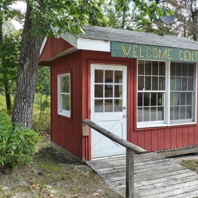 Small red welcome center cabin in a forested area with a ramp and large windows.