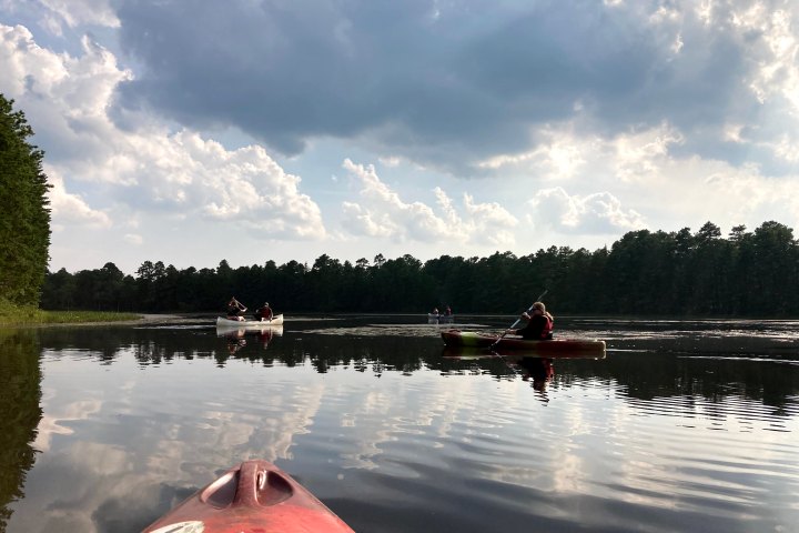 Kayaks on a calm lake under a cloudy sky surrounded by forest.